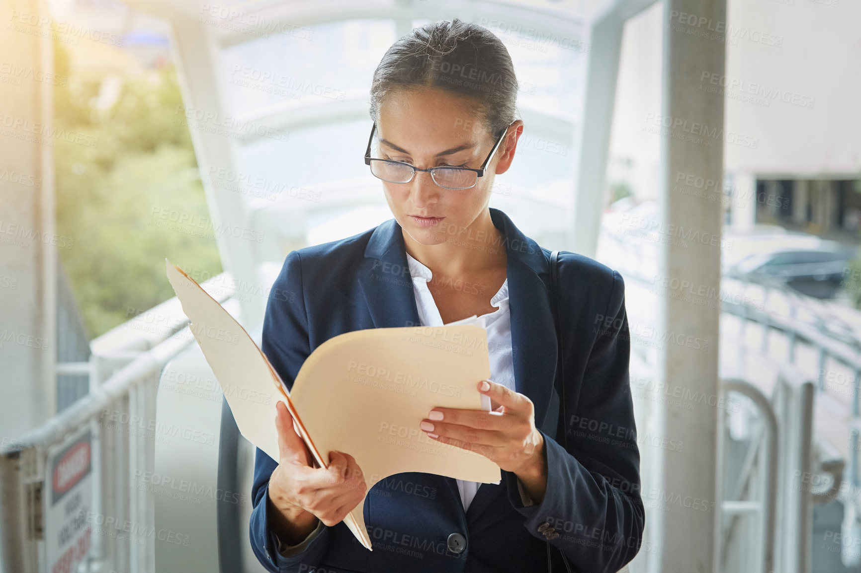 Buy stock photo Shot of a young businesswoman reading paperwork on her way to the office