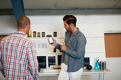 Buy stock photo Shot of a young man showing his coworker something on a mobile phone