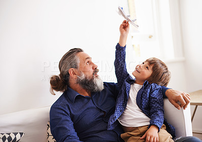Buy stock photo Cropped shot of a young boy sitting on his grandfather's lap playing with a toy jet