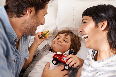 Buy stock photo Family, toys and kid playing in bedroom together for bonding, having fun and entertainment in home. Childhood development, Australian man and woman with child for joke, laughing and relax on bed