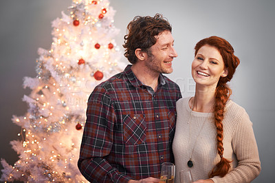 Buy stock photo Love, smile and wine with couple at Christmas to decorate to tree in studio on gray background. Alcohol, celebration or festive portrait with happy man and woman together for December holiday season