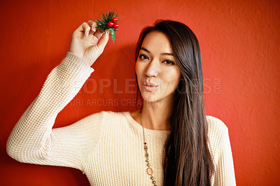 Buy stock photo An attractive young woman holding up a holly branch and blowing a kiss