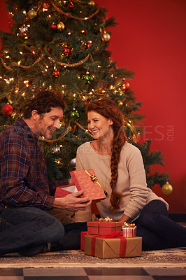 Buy stock photo Couple, tree for Christmas and gift for holiday celebration, festive season of giving for love and commitment. Happy, gratitude and support with people at home for present, romance and relationship