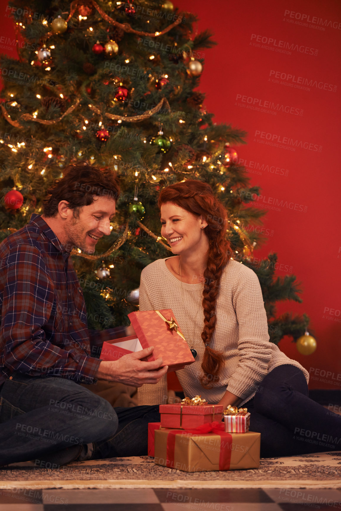 Buy stock photo Couple, tree for Christmas and gift for holiday celebration, festive season of giving for love and commitment. Happy, gratitude and support with people at home for present, romance and relationship