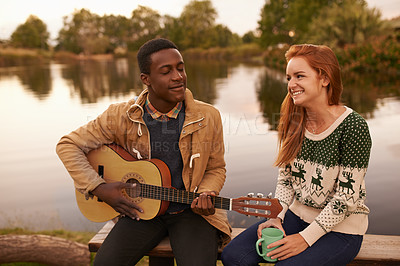 Buy stock photo Shot of a teenage boy serenading a beautiful girl while sitting beside a lake