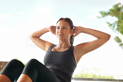Buy stock photo Shot of a sporty young woman doing sit-ups outside