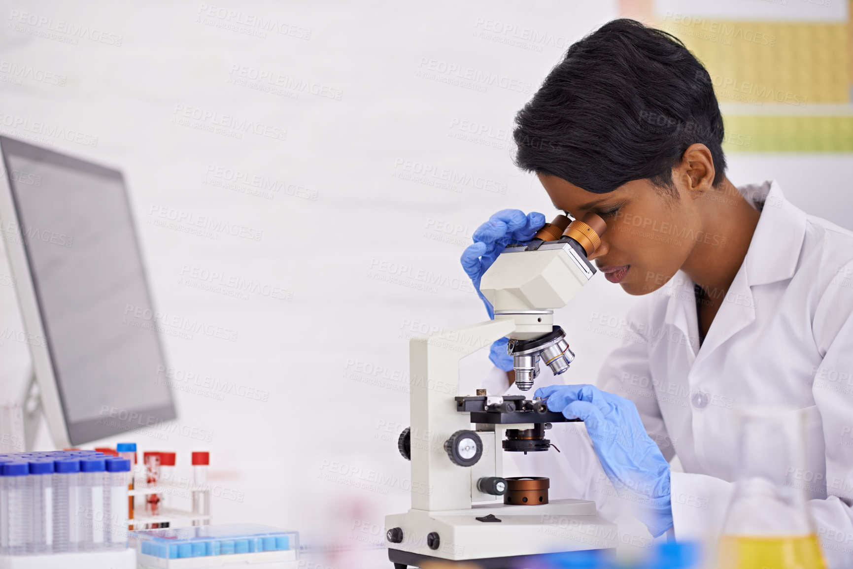 Buy stock photo A young scientist using a microscope at her desk in her lab