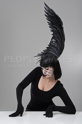 Buy stock photo Shot of a young woman in a wing-shaped headpiece sitting in a studio