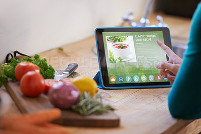 Buy stock photo Cropped shot of a young woman looking at an online recipe on her digital tablet while preparing a meal