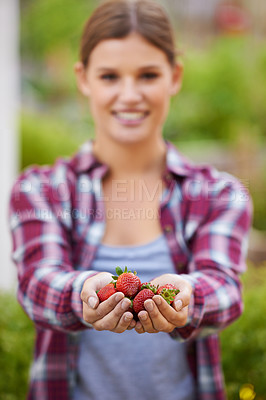 Buy stock photo Cropped shot of a happy young woman holding a handful of fresh strawberries