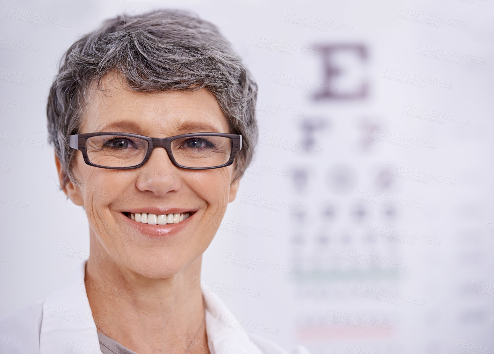 Buy stock photo Portrait of a female optometrist standing beside an eye test poster