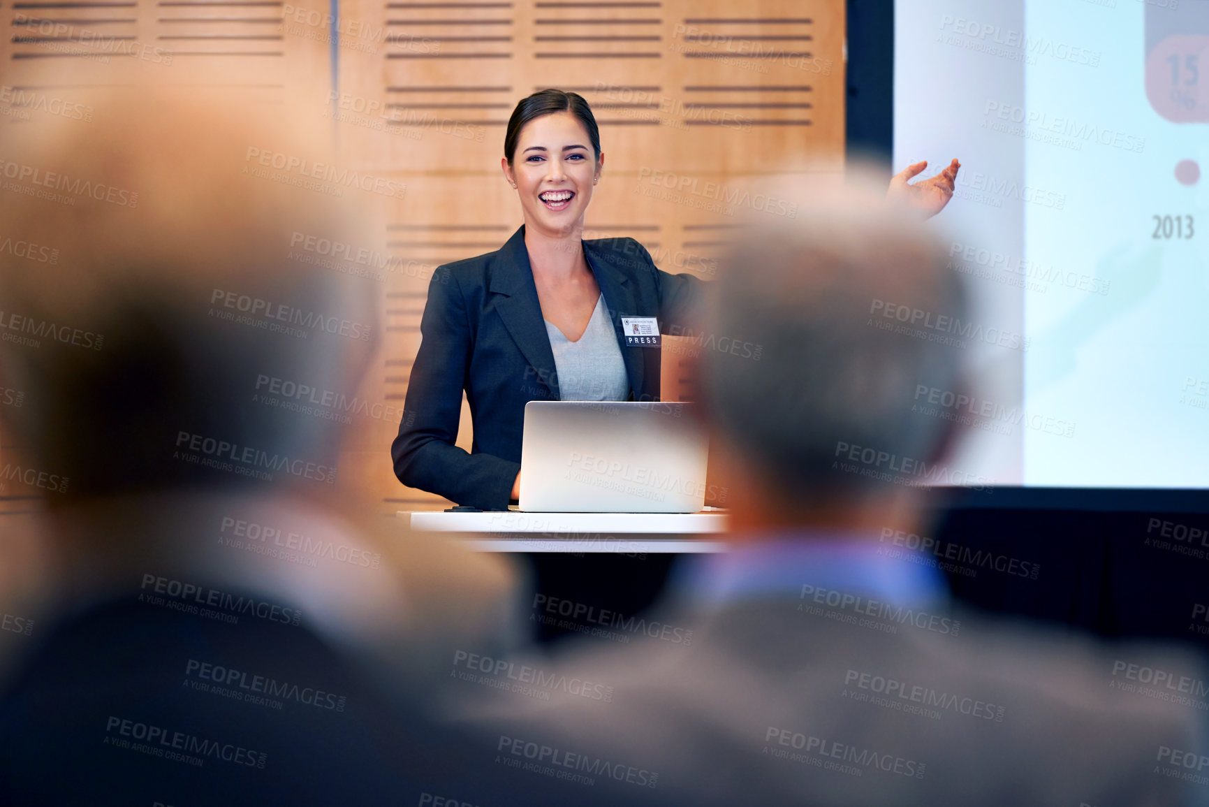 Buy stock photo A happy young businesswoman gesturing while giving a presentation at a press conference