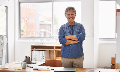 Buy stock photo Portrait of a mature businessman standing with his arms folded behind his desk