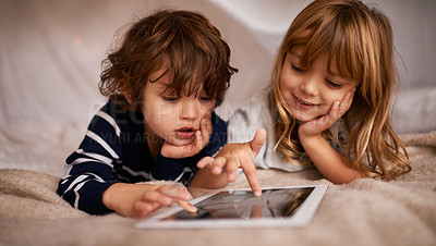 Buy stock photo Shot of two adorable siblings using a digital tablet while lying on a bed