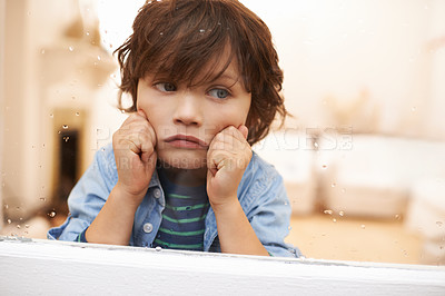 Buy stock photo Shot of an unhappy-looking little boy sitting and looking out a window on a rainy day