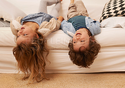 Buy stock photo Shot of two young children lying on a sofa with their heads hanging over the edge