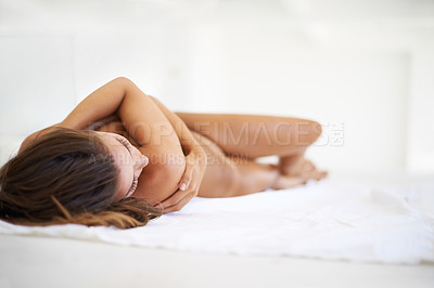 Buy stock photo Shot of a beautiful nude woman lying on a bed hugging her arms across her chest