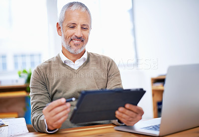 Buy stock photo A happy businessman using a tablet at his desk at work