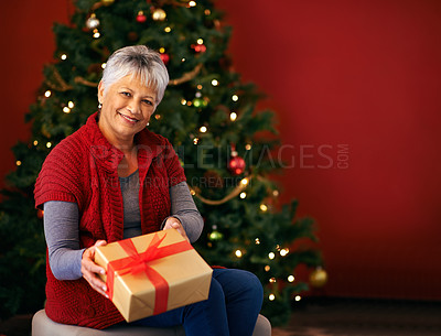 Buy stock photo Cropped shot of a woman in front of a Christmas tree offering a present