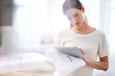 Buy stock photo Cropped shot of a young businesswoman holding a digital tablet and going through paperwork