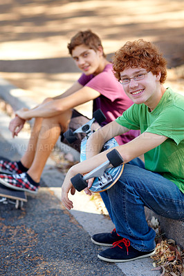 Buy stock photo Portrait of two young skateboarders sitting beside a road
