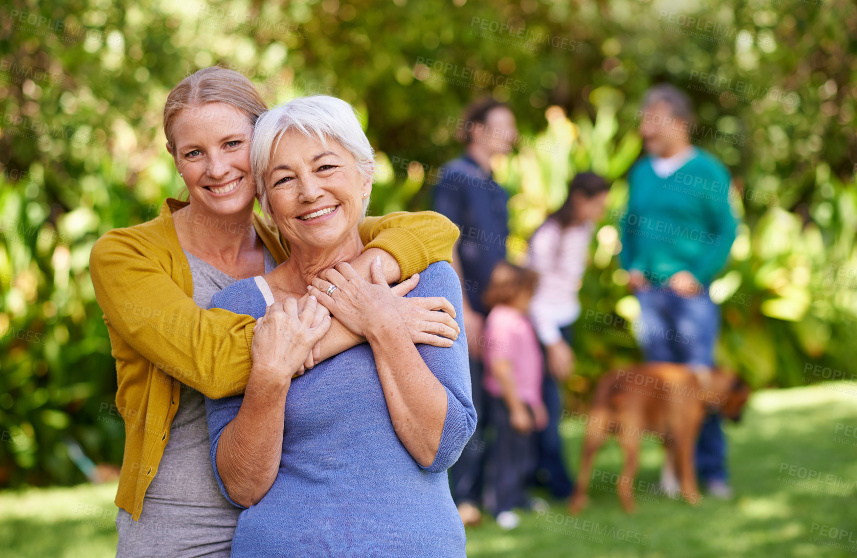 Buy stock photo Shot of a mother and her adult daughter with family in the background