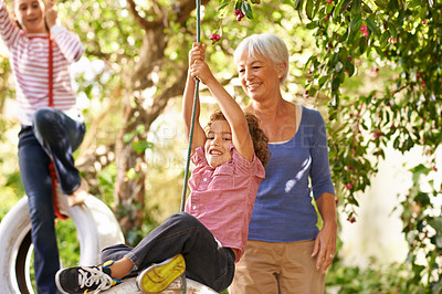 Buy stock photo Shot of a woman helping her grandson on a tire swing with her granddaughter in the background