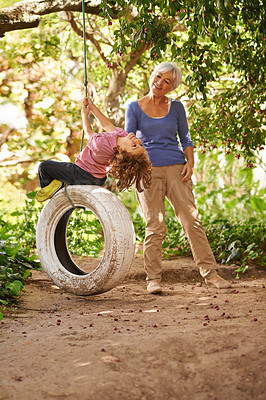 Buy stock photo Elderly woman, garden and grandchild playing with grandma or holidays and having fun on a tyre swing in summer. Excited, grandkid and outdoors on jungle gym together or on sunny weekend at a park