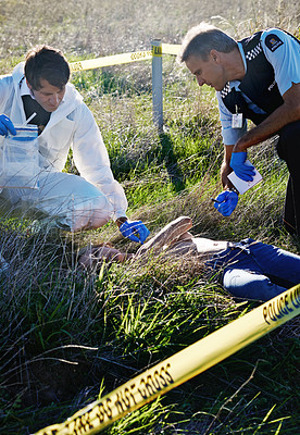 Buy stock photo Shot of two investigators searching the body for evidence at a murder scene