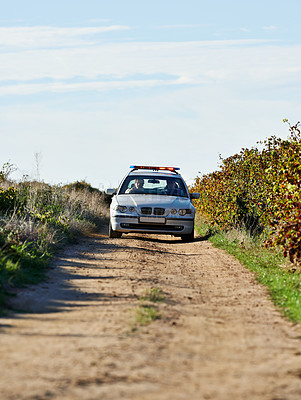 Buy stock photo Shot of a police car driving down a dirt road