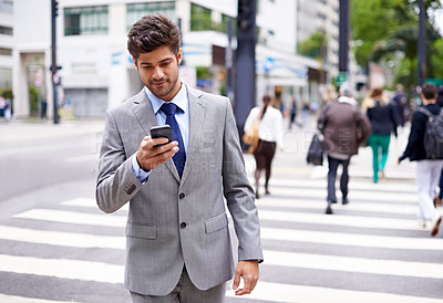 Buy stock photo A cropped shot of a handsome young businessman texting while walking in the city