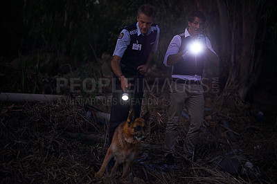 Buy stock photo Shot of two policemen and their canine tracking a suspect through the brush at night