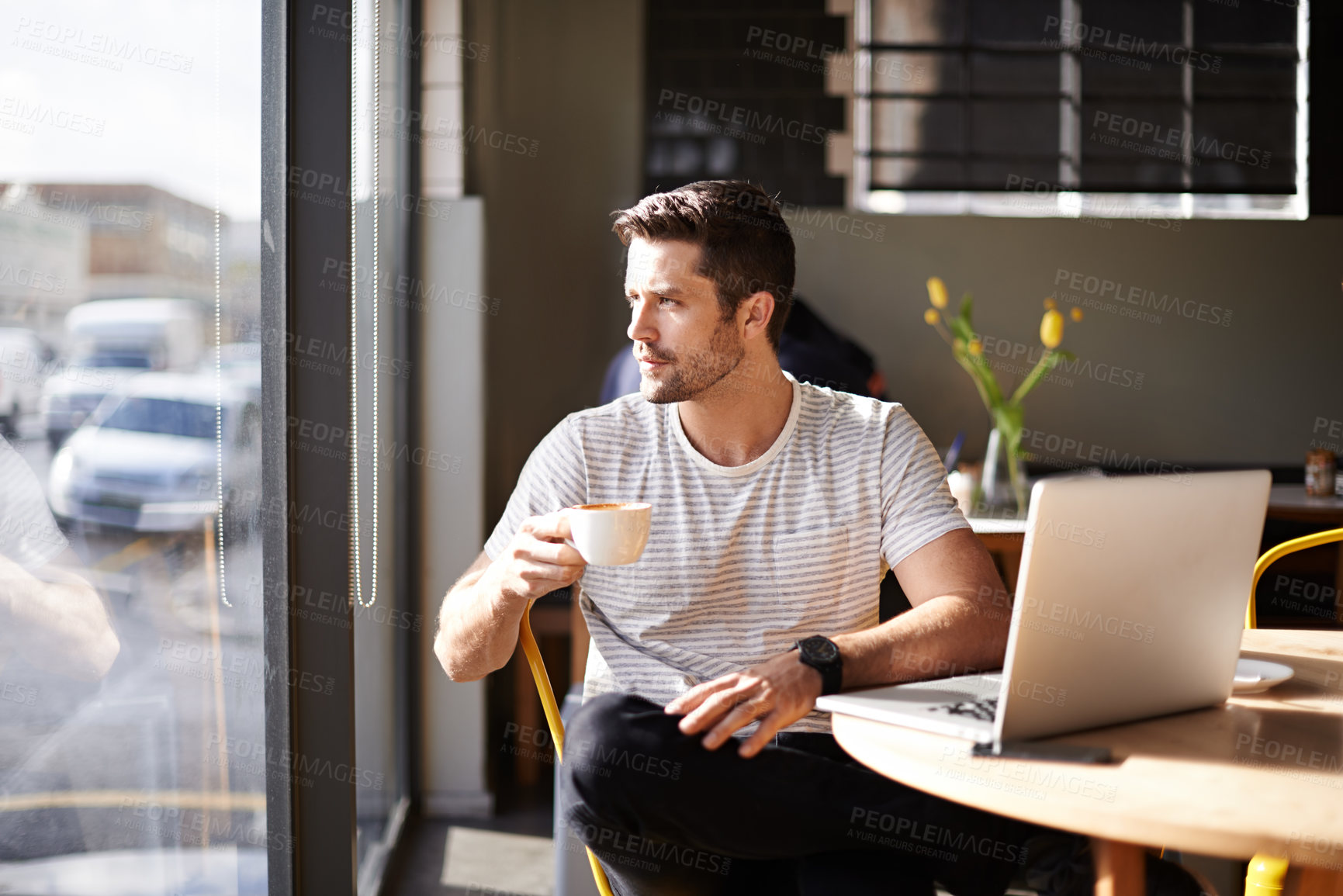 Buy stock photo Shot of a young man working on a laptop in a cafe and drinking coffee