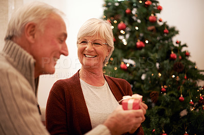 Buy stock photo Senior couple, giving gift and together for Christmas holiday celebration at home with a smile, happiness and kindness. Surprise, celebrate and tree with man and woman holding a present and gift box