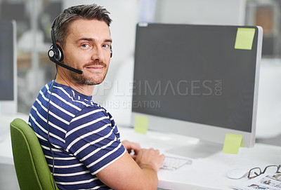 Buy stock photo Shot of a young businessman wearing a headset while working at his desktop computer