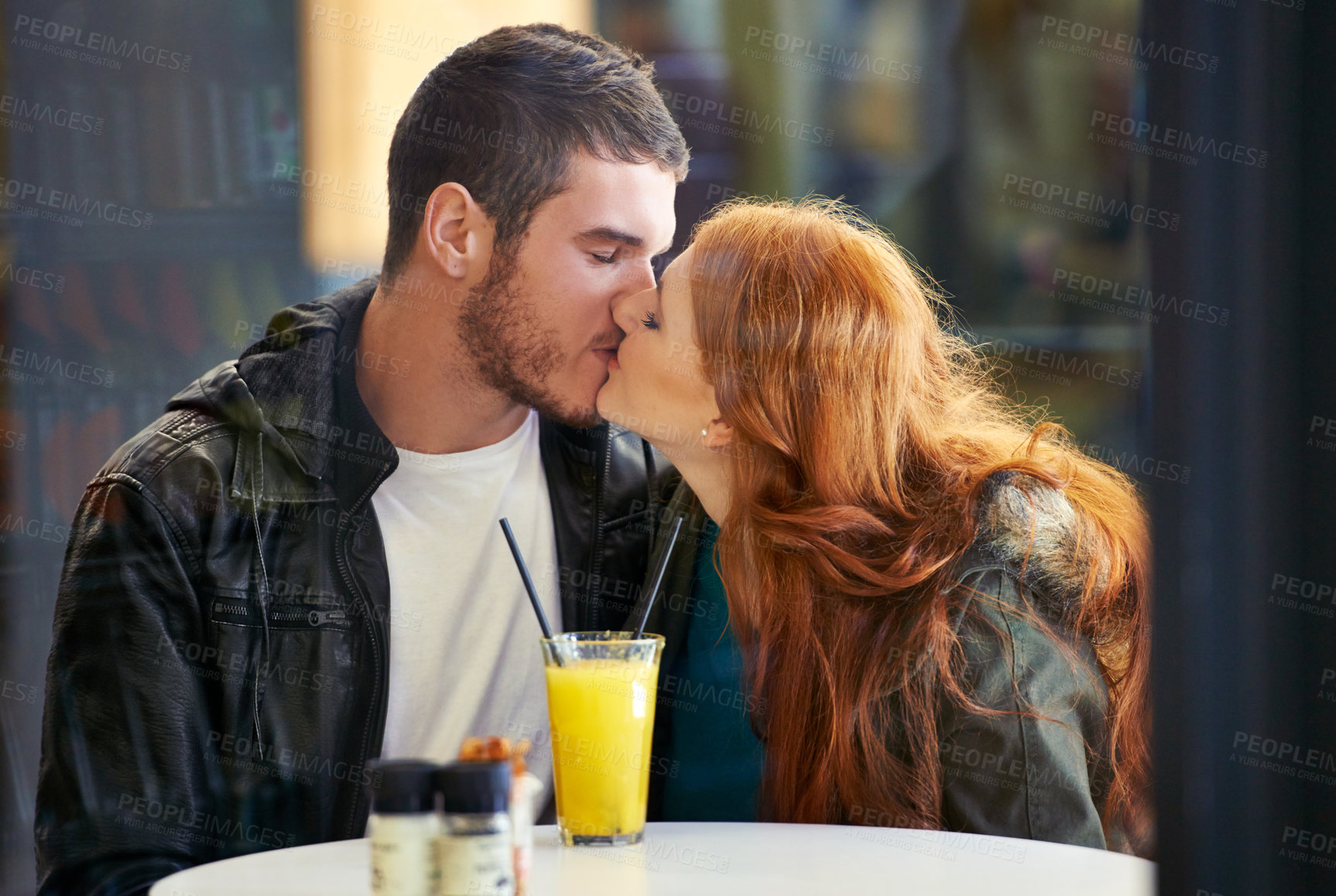 Buy stock photo Couple, date and kiss with romance, cafe or restaurant with orange juice and happiness together. Man, woman and love for relationship, care and smile for flirting on break for relax or bonding