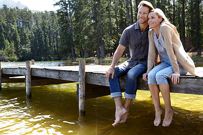 Buy stock photo Couple, lake and sitting on pier, outdoor and happy for hug on vacation, relax or memory in summer. Man, woman and embrace with smile, care or bonding with connection for love on holiday in Colorado