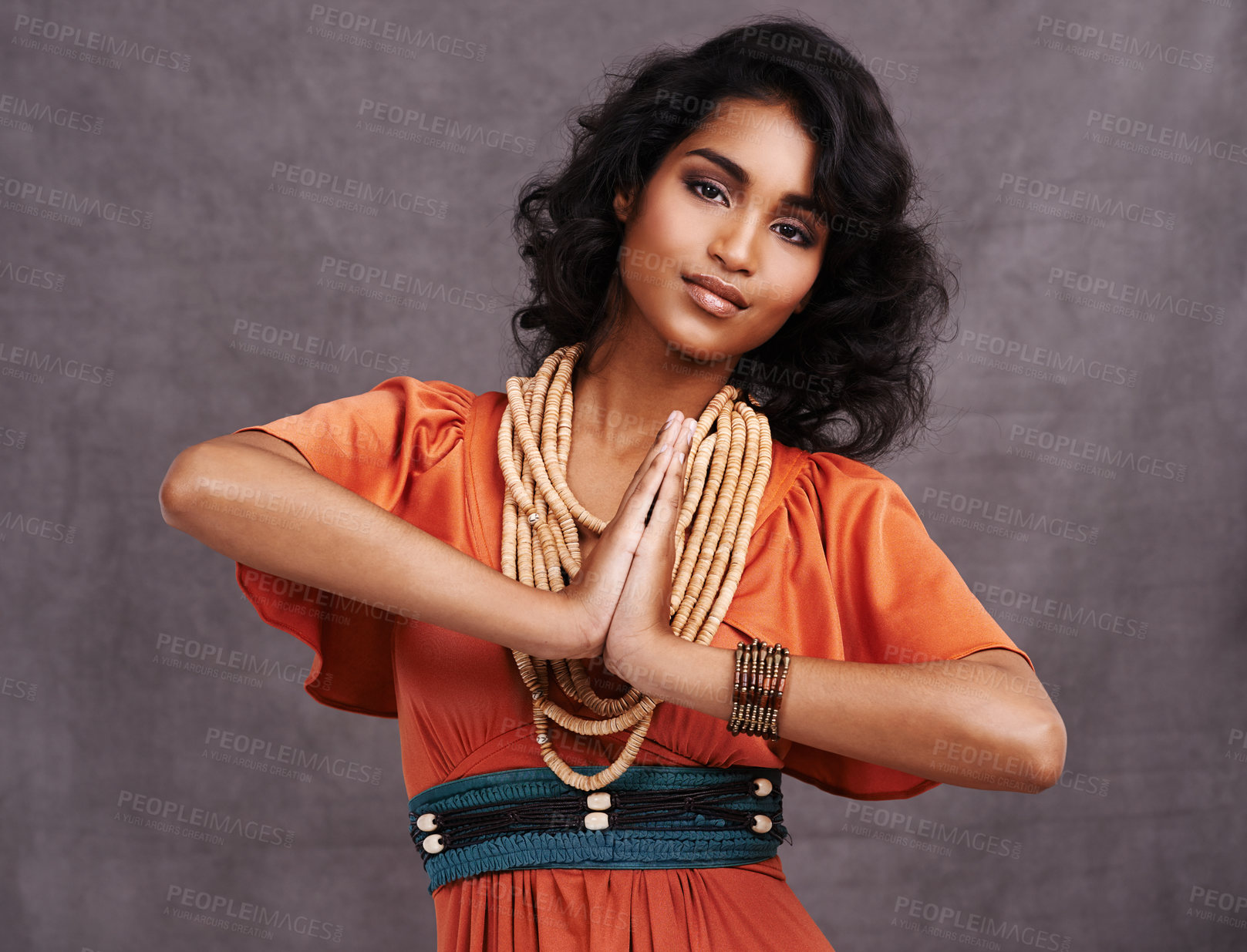 Buy stock photo Indian woman, fashion and smile with jewelry in studio on grey background with hands together and dress. Portrait, female person and outfit with confidence in traditional necklace and creative look