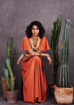 Buy stock photo Studio portrait of a beautiful young ethnic woman sitting amongst cacti against a gray background