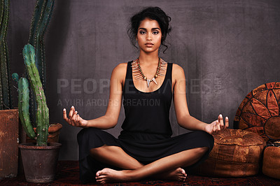Buy stock photo Studio portrait of a beautiful young woman sitting in the lotus position beside a cactus and cushions