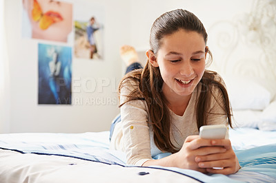 Buy stock photo Shot of a teenage girl lying on her bed and texting on her phone