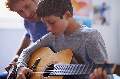 Buy stock photo Shot of a boy learning to play guitar from his father
