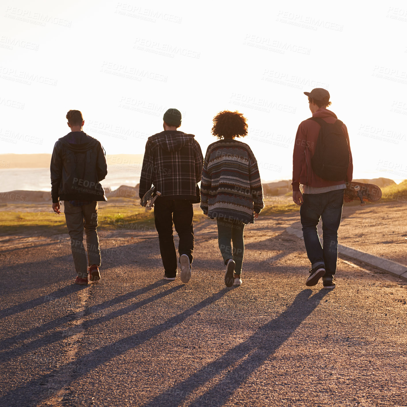 Buy stock photo Walking, sunset and back of friends on vacation, travel or holiday together with skateboard. Summer, evening and group of young people by outdoor ocean or sea on weekend trip for bonding in nature.