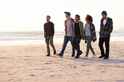 Buy stock photo Shot of a group of friends walking along a beach at sunset