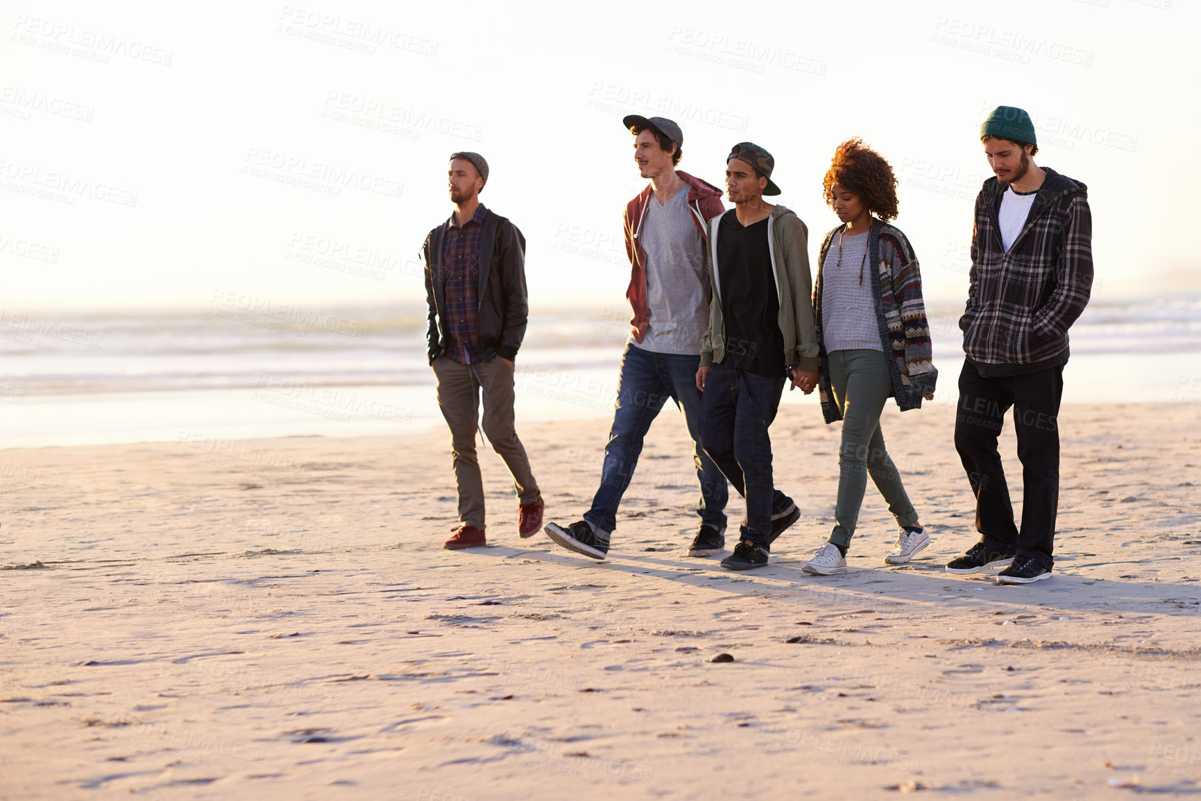 Buy stock photo Shot of a group of friends walking along a beach at sunset