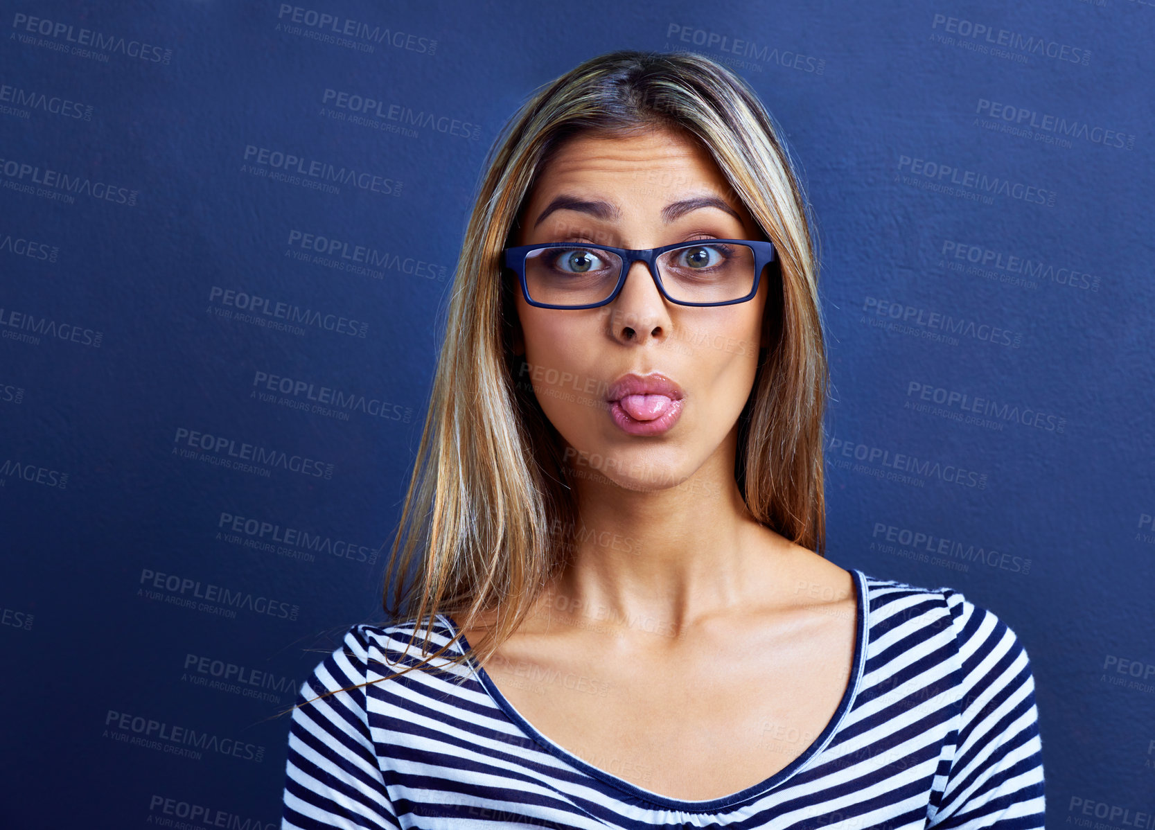 Buy stock photo Funny, face and woman with glasses in studio for tongue out, silly or humor on blue background. Need, portrait and female model with emoji expression, gesture or geek, aesthetic or quirky personality