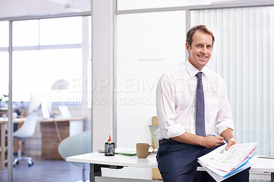 Buy stock photo Portrait of a handsome young businessman reading through documents in his office