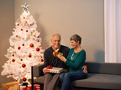 Buy stock photo Shot of a happy mature couple exchanging gifts on Christmas eve
