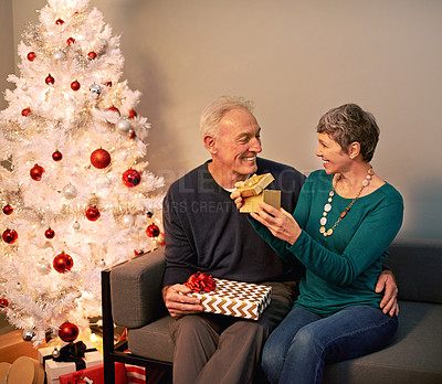 Buy stock photo Christmas, gift and senior couple with love, holiday giving and support together in home with romance. Happy, retirement and marriage with smile and hug in house with celebration and presents