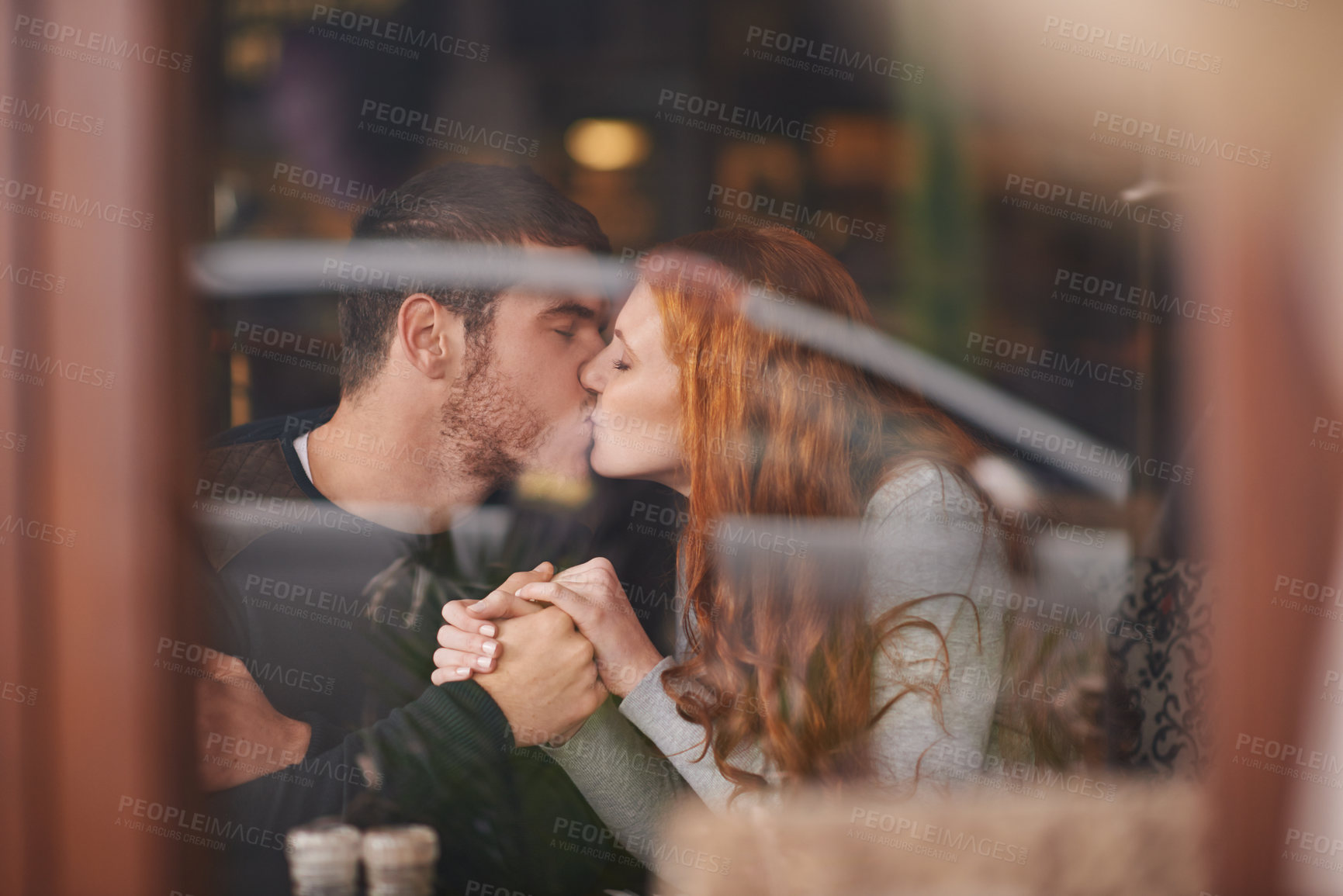 Buy stock photo Couple, kissing and holding hands on date at cafe for bonding, romance and healthy relationship with relax. Man, woman and affection at coffee shop with lens flare, trust and love on anniversary trip